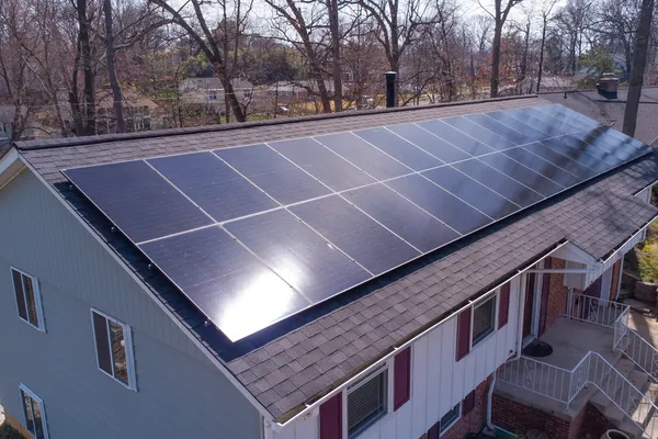 Aerial view of a residential home with rooftop solar panels installed, surrounded by trees in a suburban neighborhood